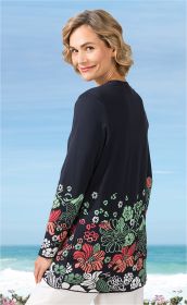 Frau trägt dunkelblaue Baumwoll-Strickjacke mit buntem floralen Muster am Saum und Ärmeln, blickt lächelnd über die Schulter, dahinter Strand und Meer bei klarem Himmel