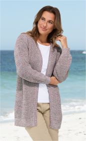 Frau trägt leichte mehrfarbige Baumwoll-Strickjacke mit offenem Schnitt, weiße Bluse, helle Hose, steht am Strand mit Meer im Hintergrund, lächelnd, eine Hand leicht am Haar, helle Tageslichtaufnahme